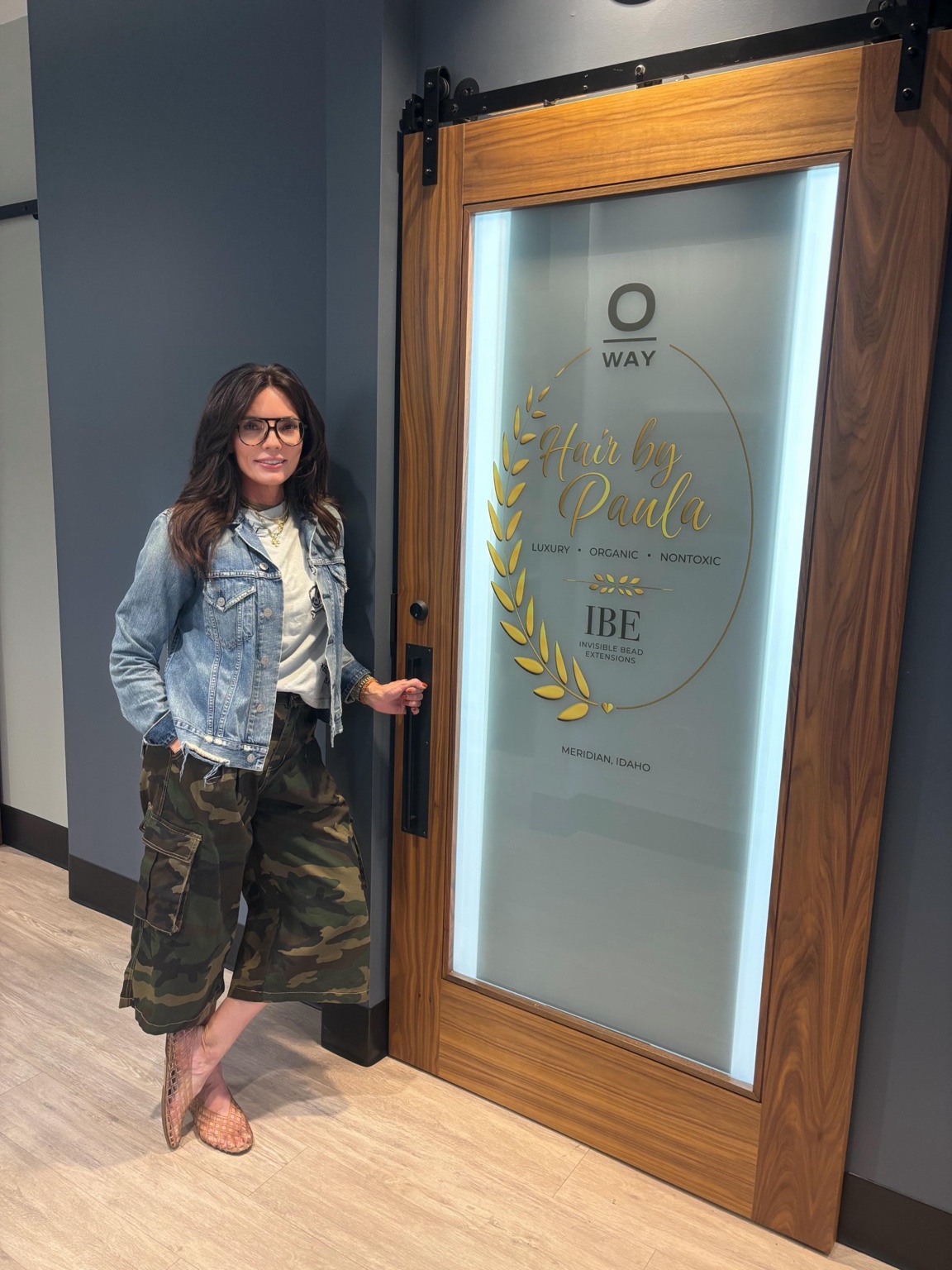 Paula Bennett standing beside the Hair by Paula OWAY and IBE salon door in Meridian